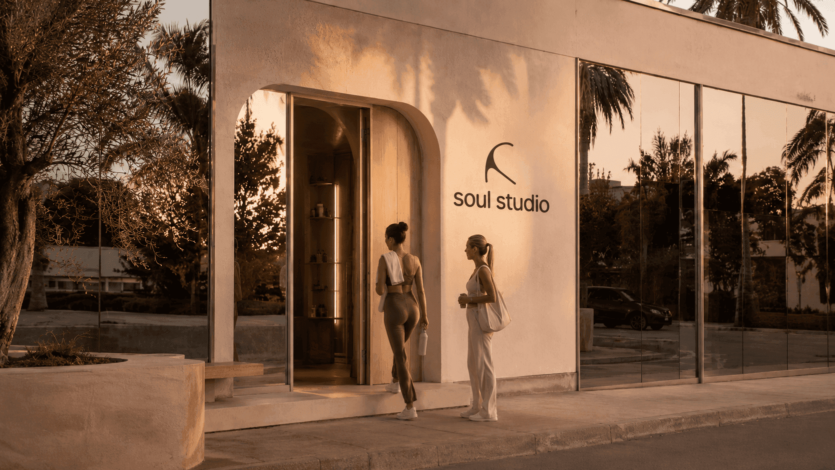 The soul studio storefront at golden hour — plaster façade, the studio wordmark, olive trees and two members at the door.